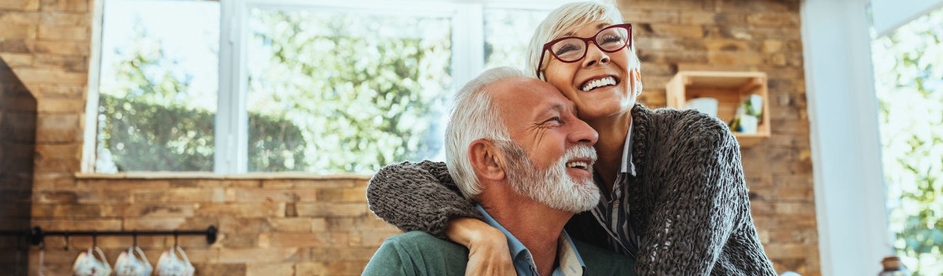 Senior Couple Smiling and Hugging at Kitchen Table