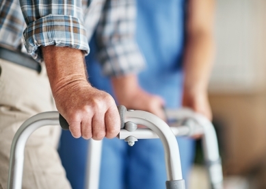 Male hands on walker with nurse in background